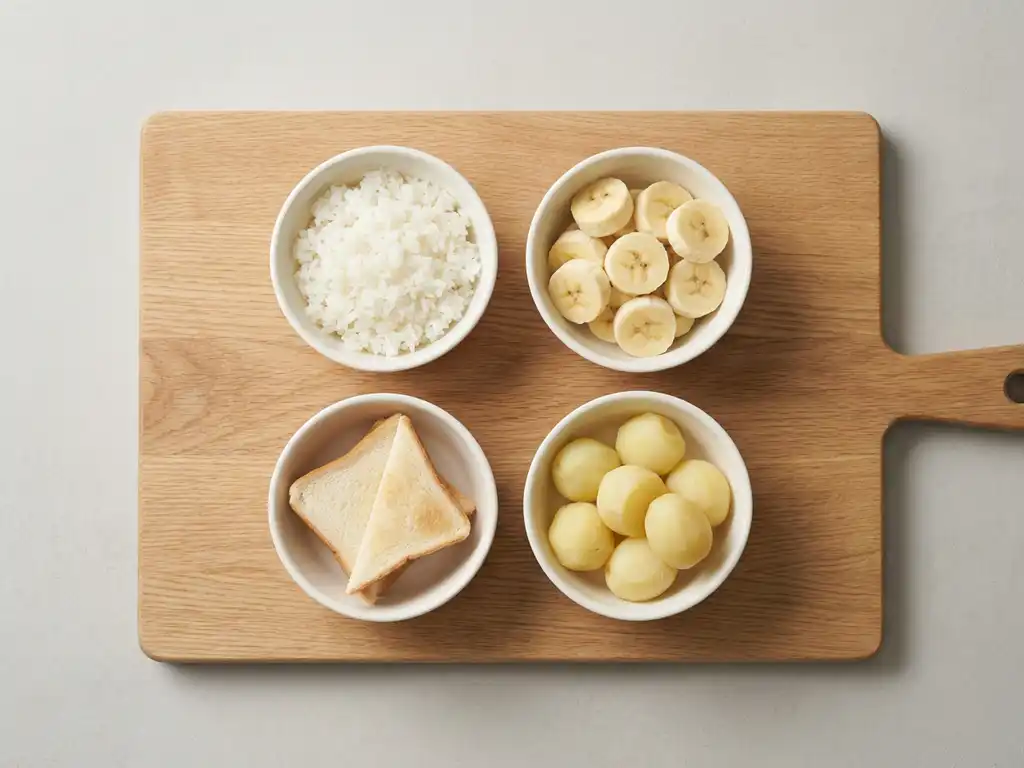 Wooden cutting board with white bowls containing gut-friendly foods: white rice, bananas, toast triangles, and boiled potatoes