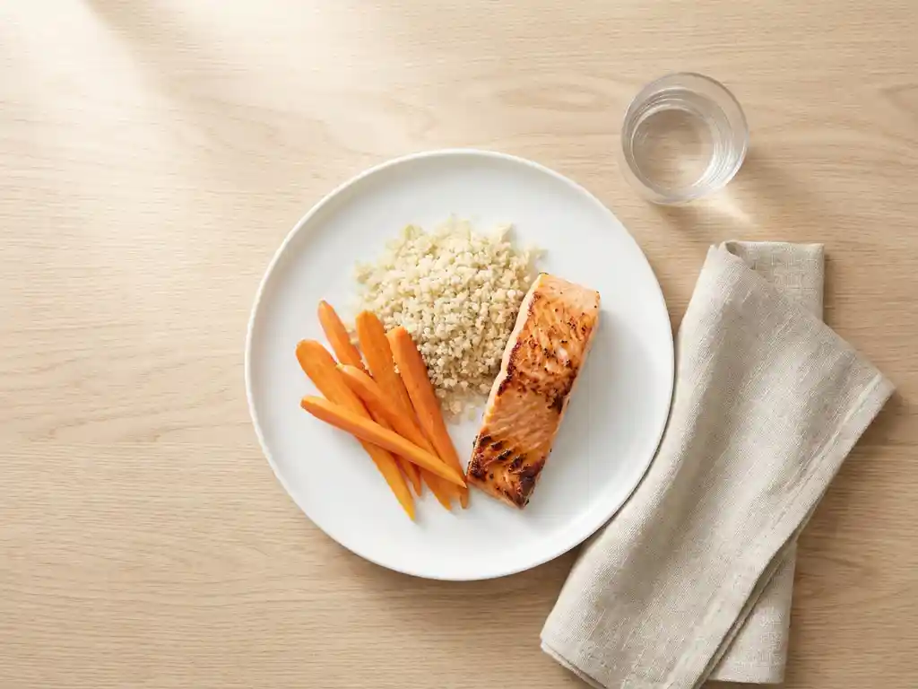 Grilled salmon with steamed carrots and quinoa on white ceramic plate, overhead view with glass of water and linen napkin